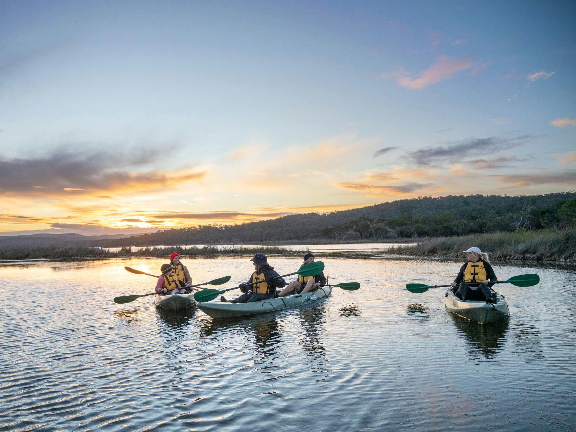Guests paddle the lake with orange sunset behind them