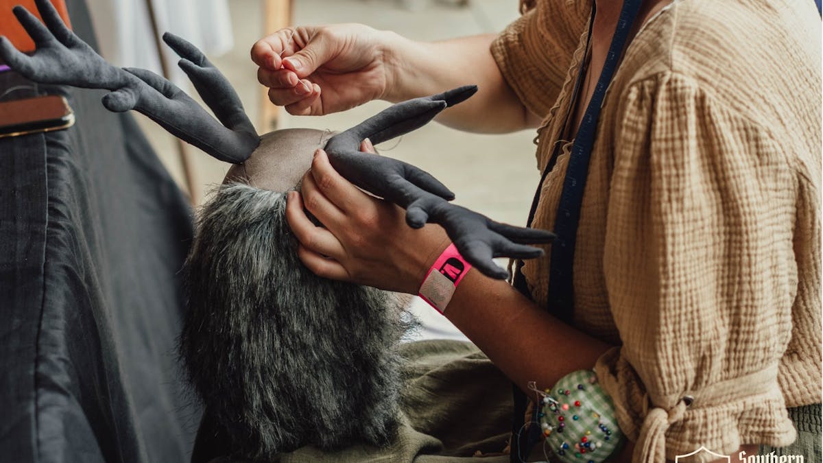 Artisan hand-stitching a plush horned headdress at Southern Realm Festival.