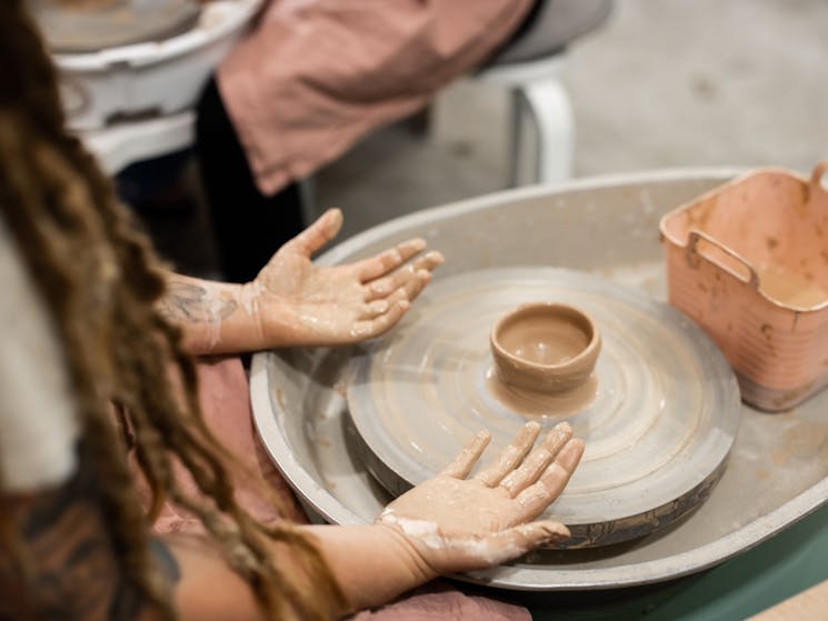 picture of hands over a pottery wheel making a clay pot