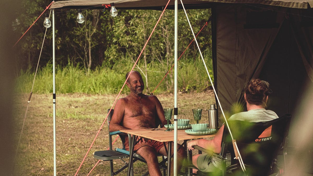 A mature couple sat outside a tent with the table set for dinner and the lights ready for evening
