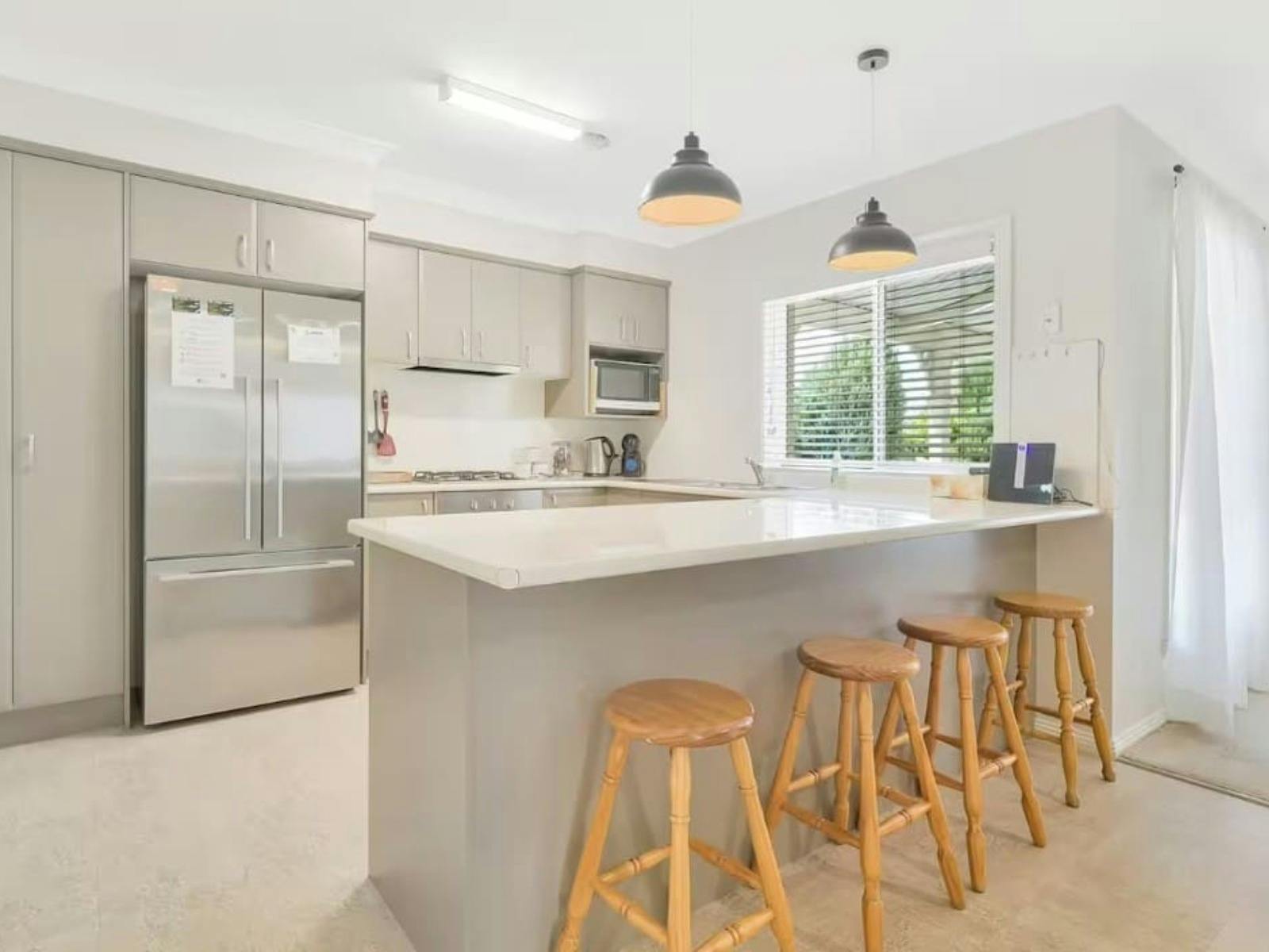 Grey kitchen with fridge and large bench with bar stools