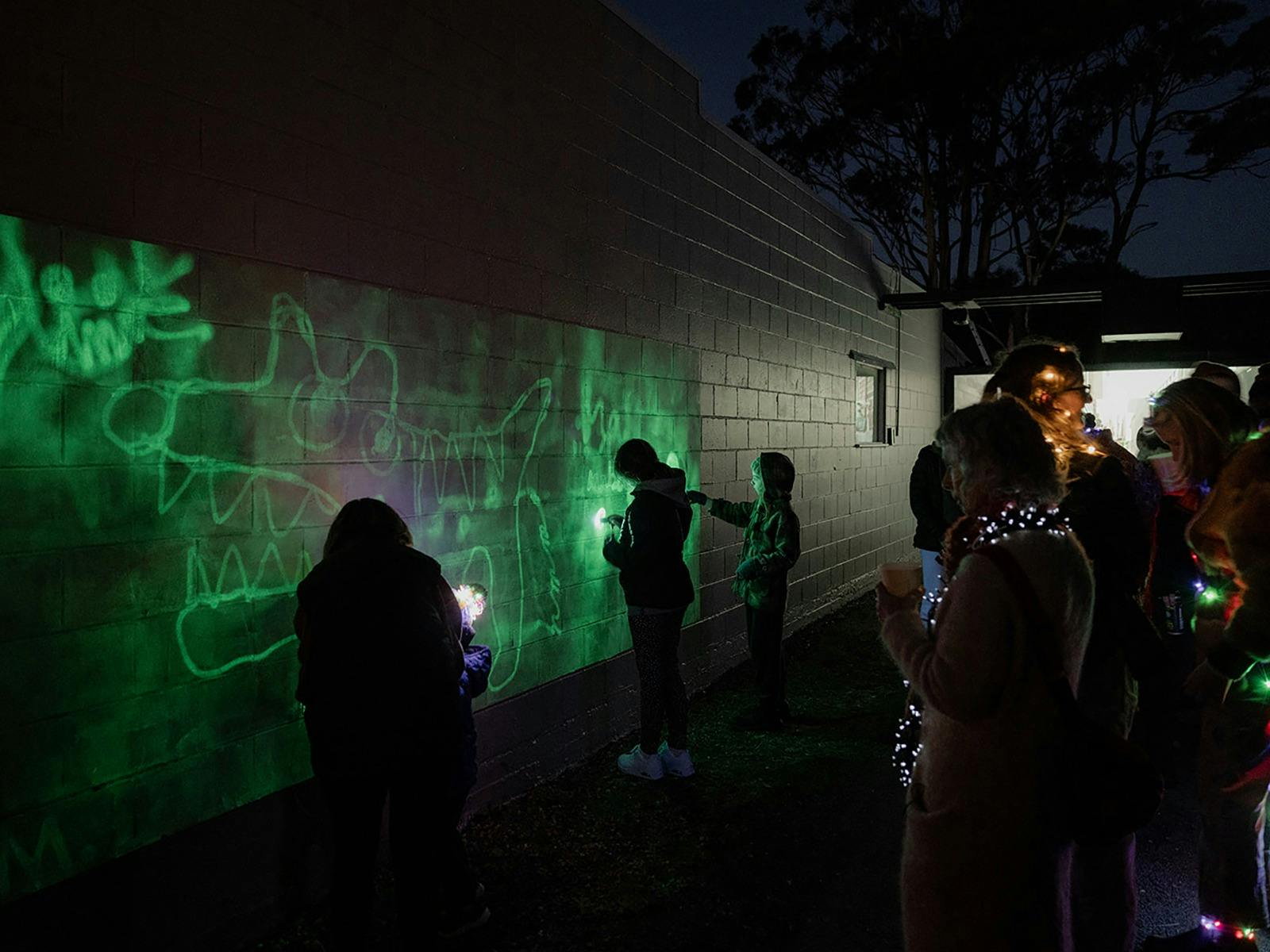 People drawing with blacklight torches creating green light drawings.