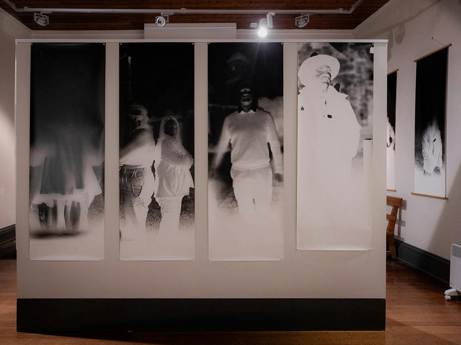 Four life-sized, black and white, inverted images of people are displayed on a white wall.