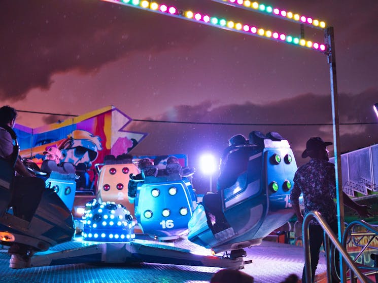 An amusement ride with colorful capsules in circular motion, people seated inside.