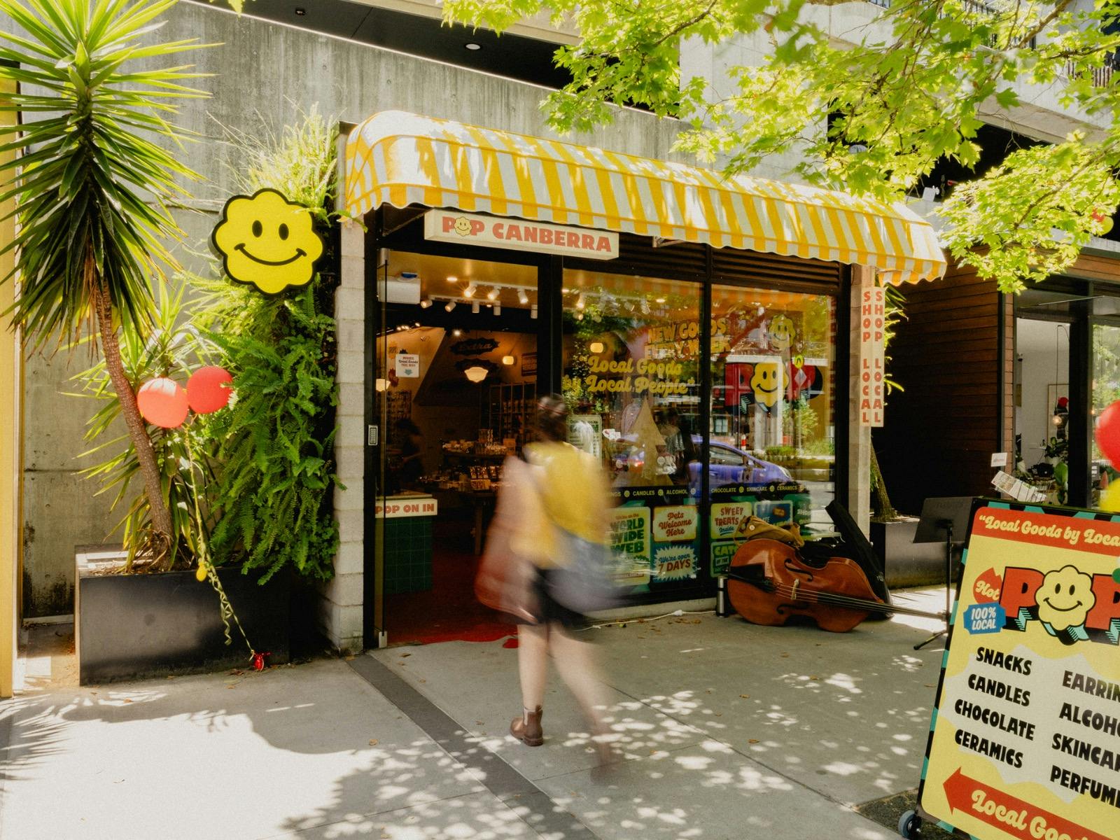 A sunny day outside POP Canberra, showcasing its bright yellow awning, cheerful signage. Welcome.