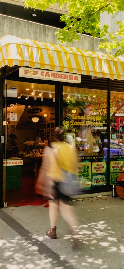 A sunny day outside POP Canberra, showcasing its bright yellow awning, cheerful signage. Welcome.
