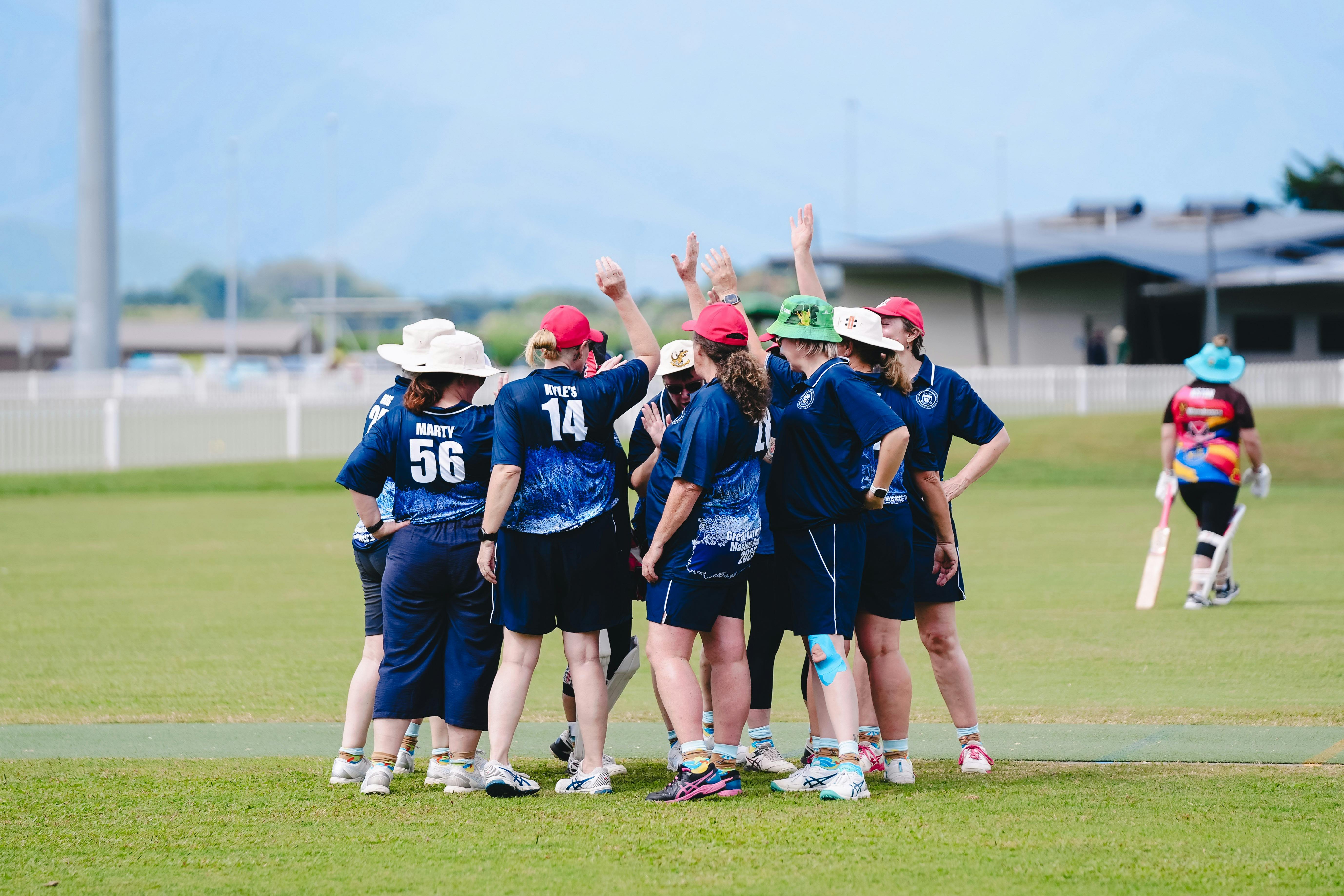 A group of cricket players huddle and high-five on a grassy field