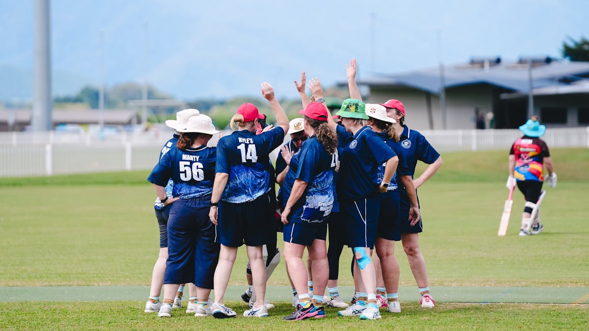 A group of cricket players huddle and high-five on a grassy field