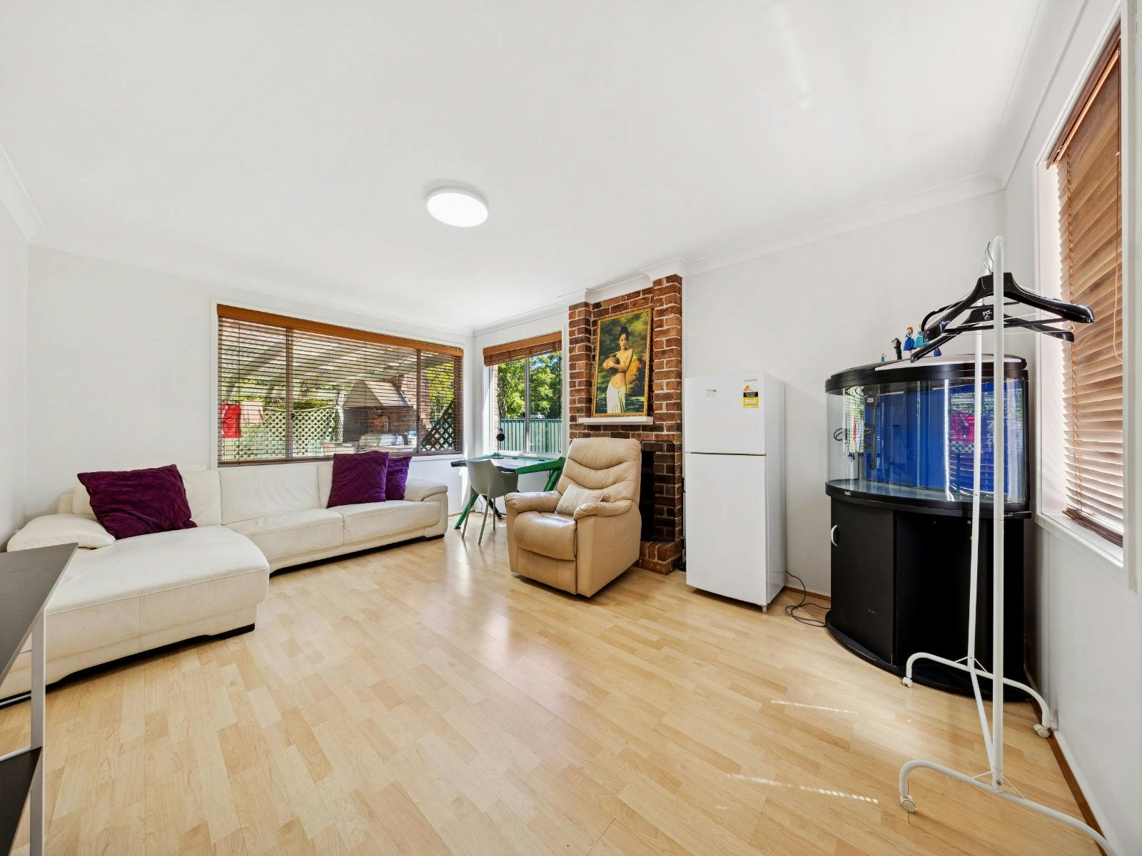Spacious light-filled living area featuring timber flooring, a white L-shaped sofa with accent chair