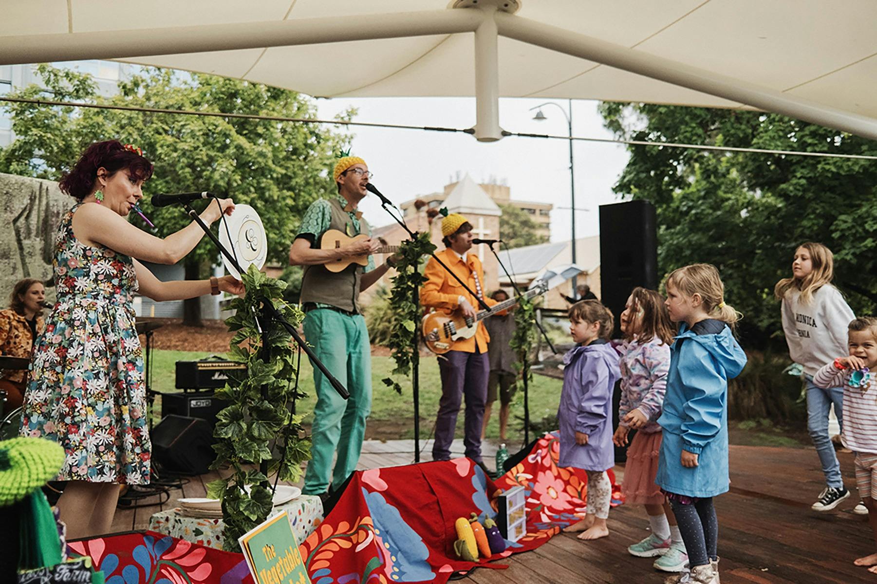 A lively outdoor children's concert with musicians in colorful outfits playing instruments.