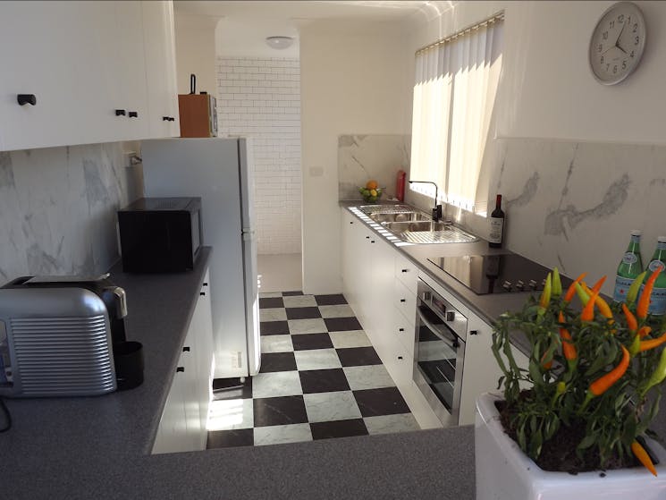 Black and white checkrboard floor tiles with white cabinets and black handles. Splashback is a marbl