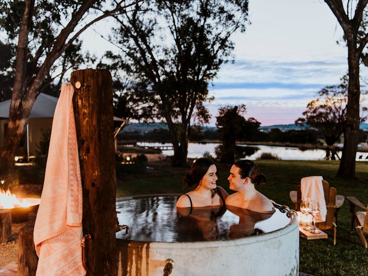 Couple relaxing in hot tub with sun setting behind them