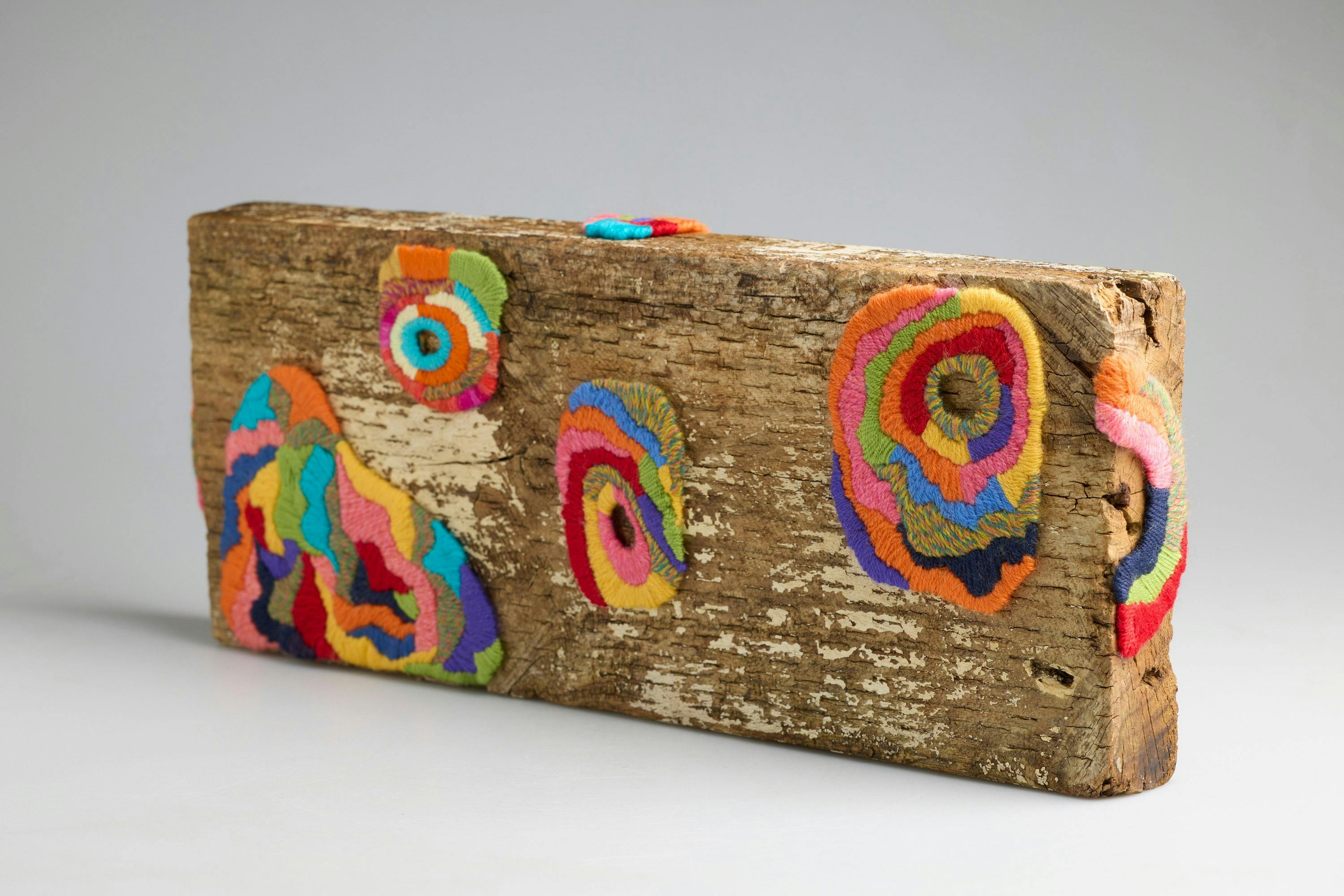 sculpture made with rectangular piece of wood with multi coloured textile swirls added to the piece