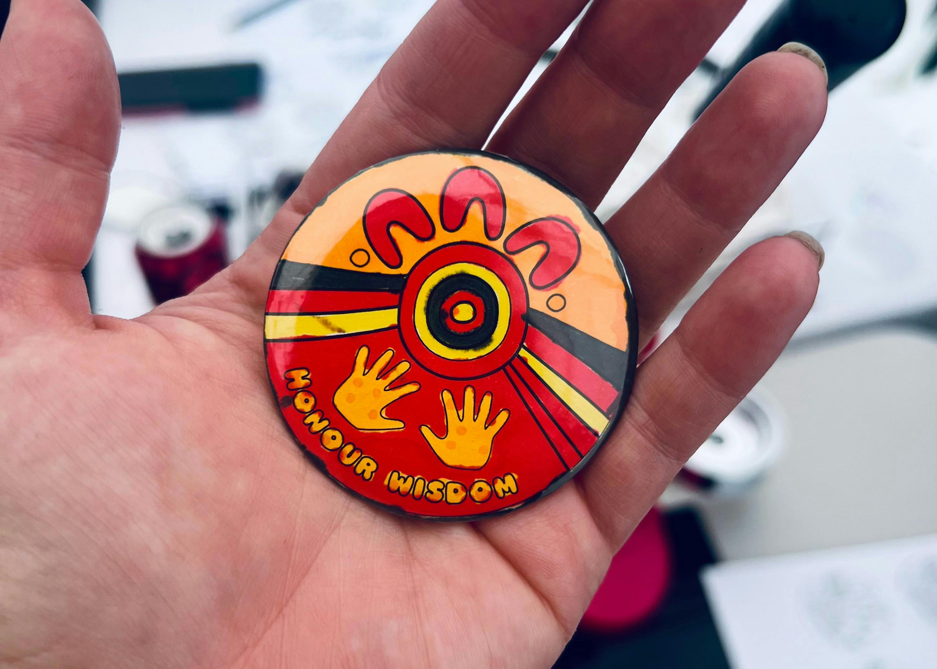 A small hand holding a colourful badge featuring First Nations artwork