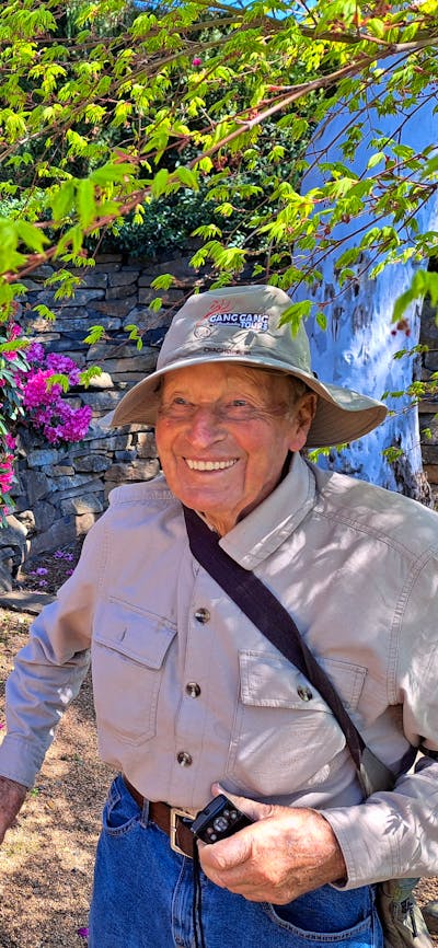 senior gentleman beside rock wall and pink blooms