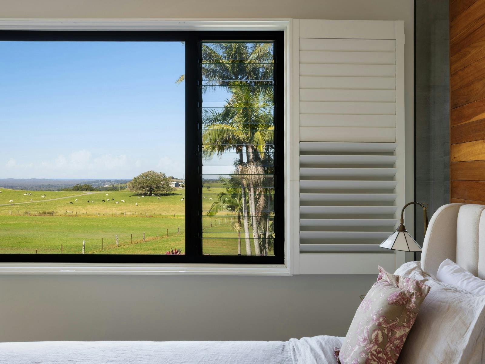 Bedroom overlooking rolling green paddocks through large picture windows.