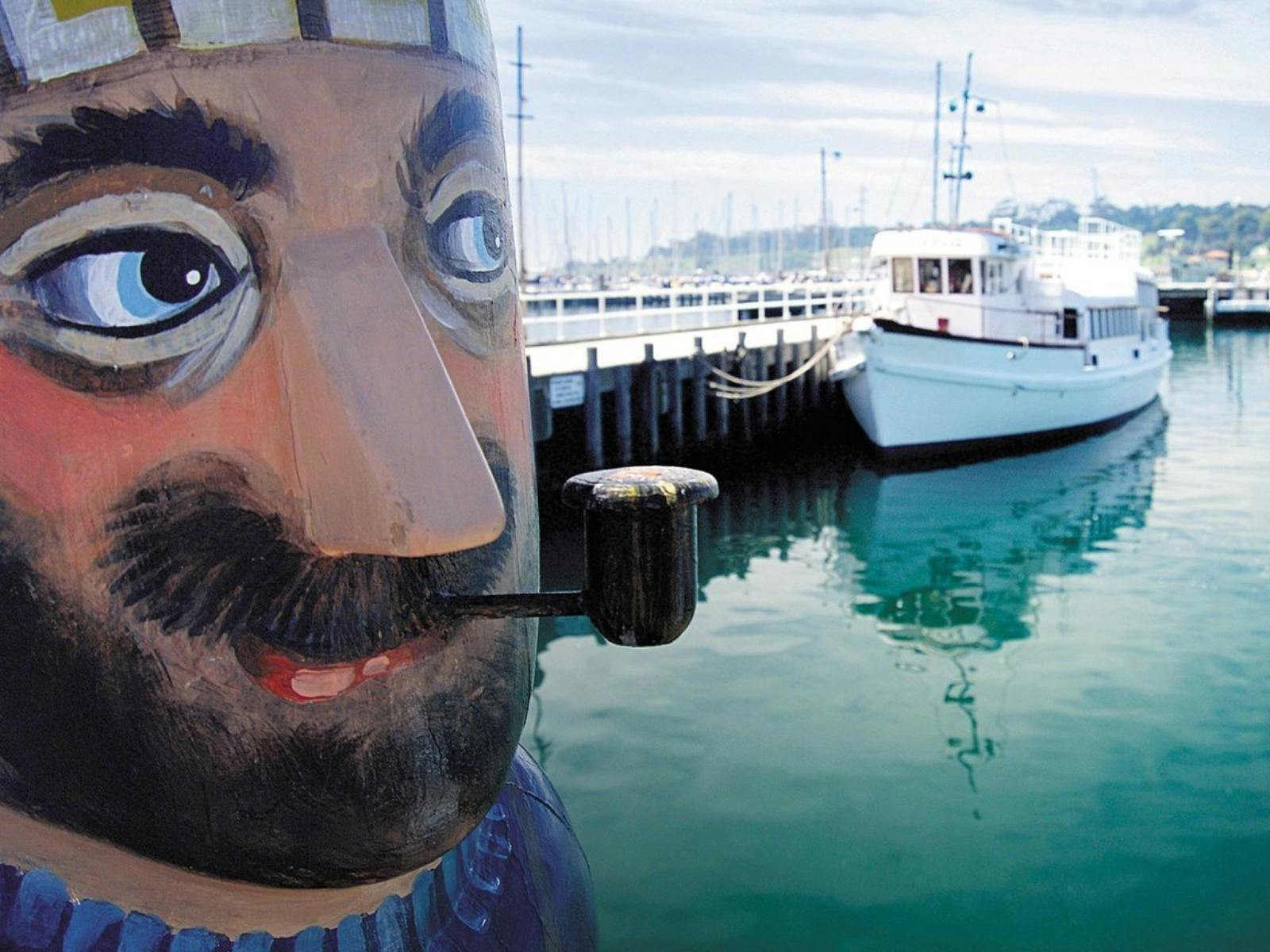 Fisherman Bollard with pipe in mouth boat in water in background