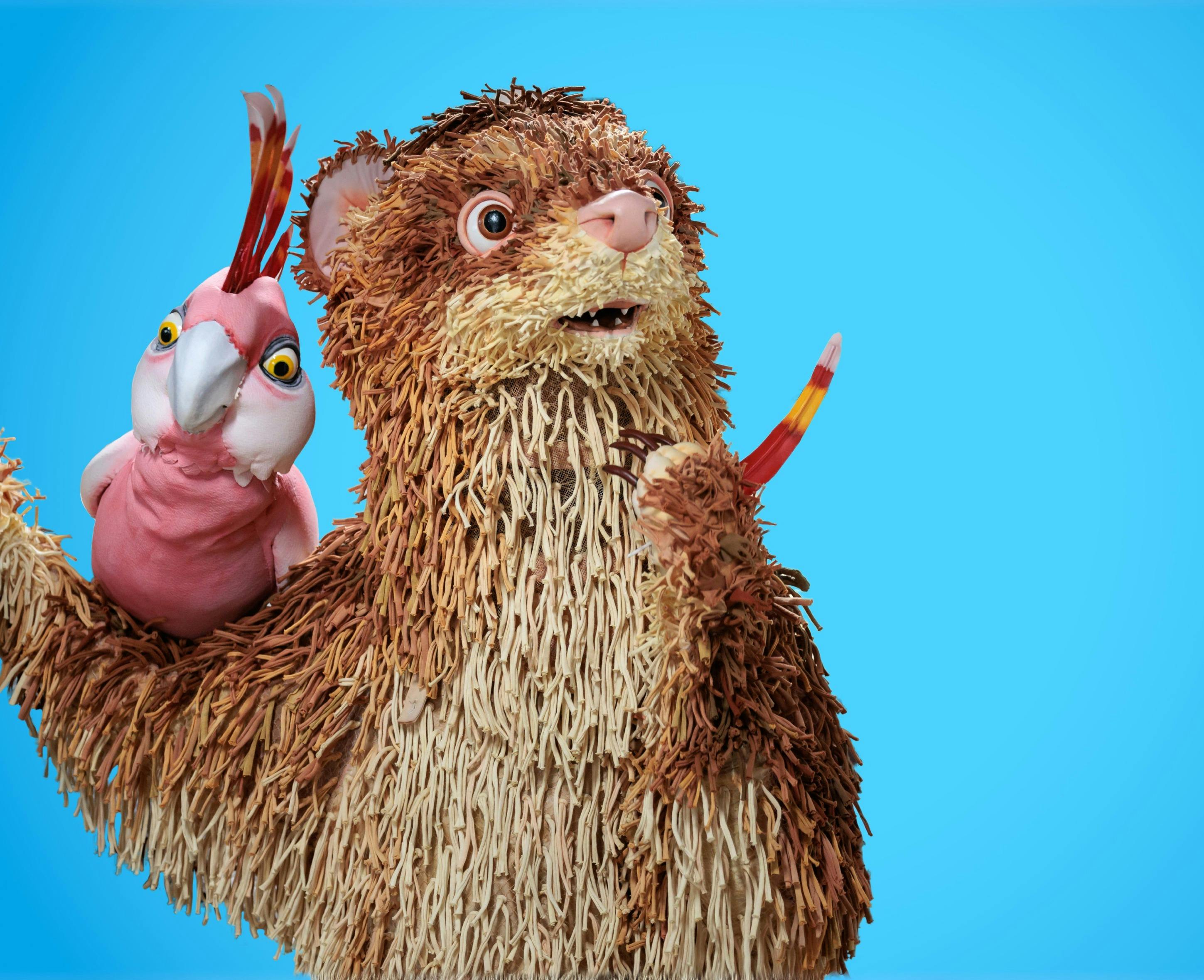 A ferret and a pink galah puppet pose against a blue background.