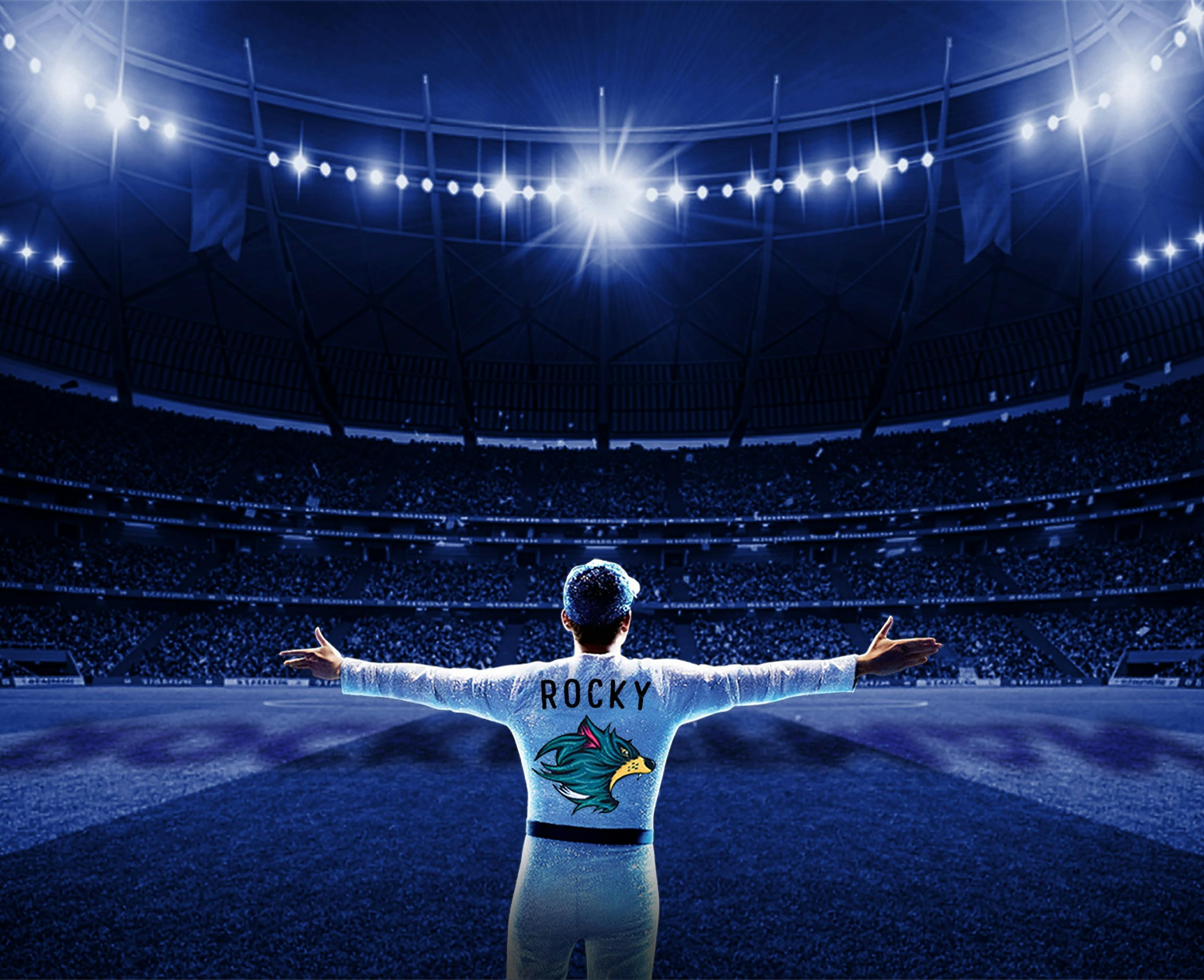 A man dressed similarly to Elton John who's jacket says "rocky" facing a crowd