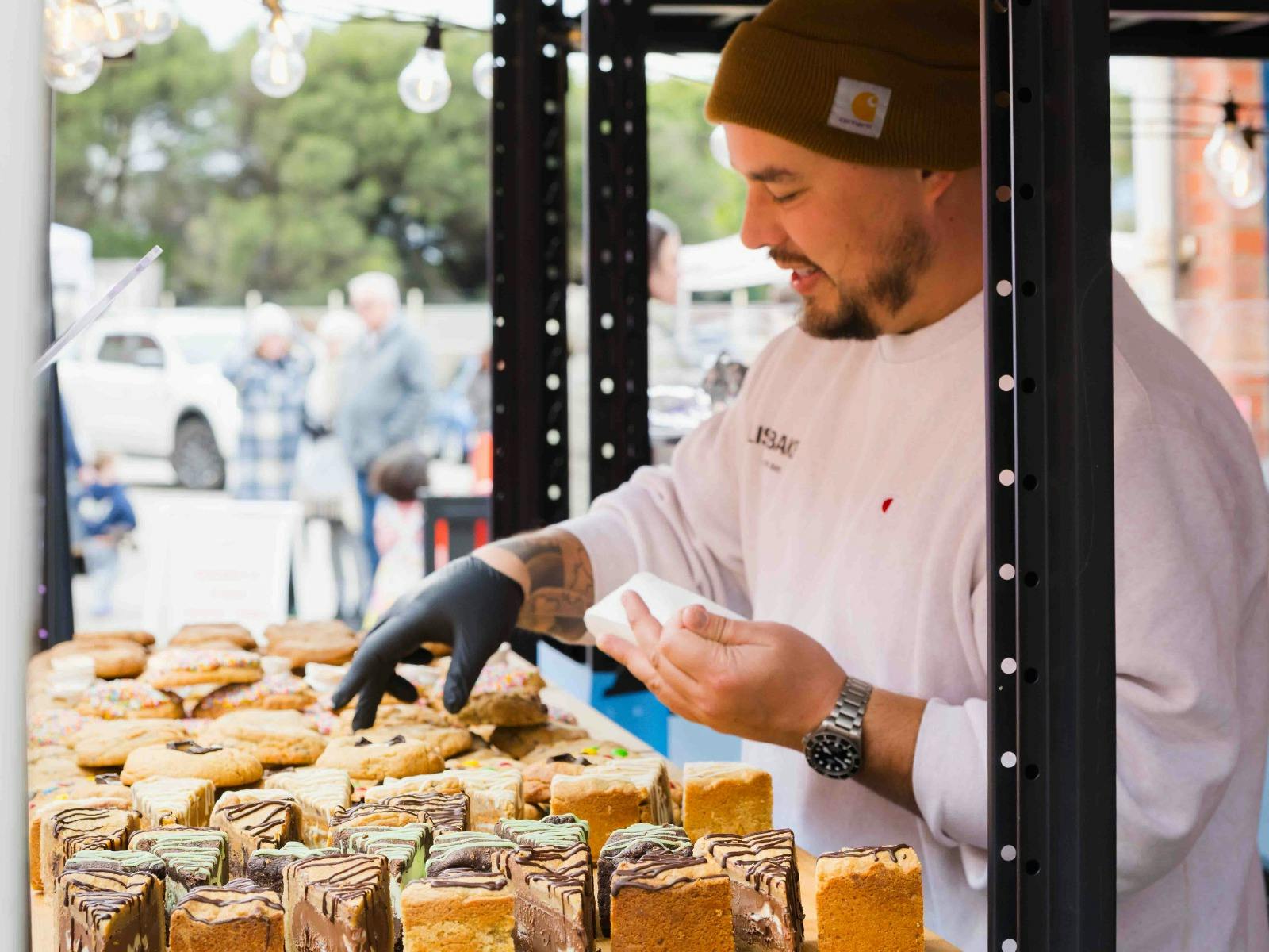 Food vendor serving baked treats at a busy outdoor community market.