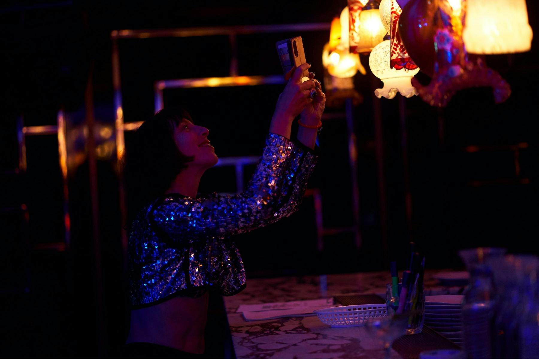 A stylish young woman relishes the moment by photographing the vintage lamps above the bar.