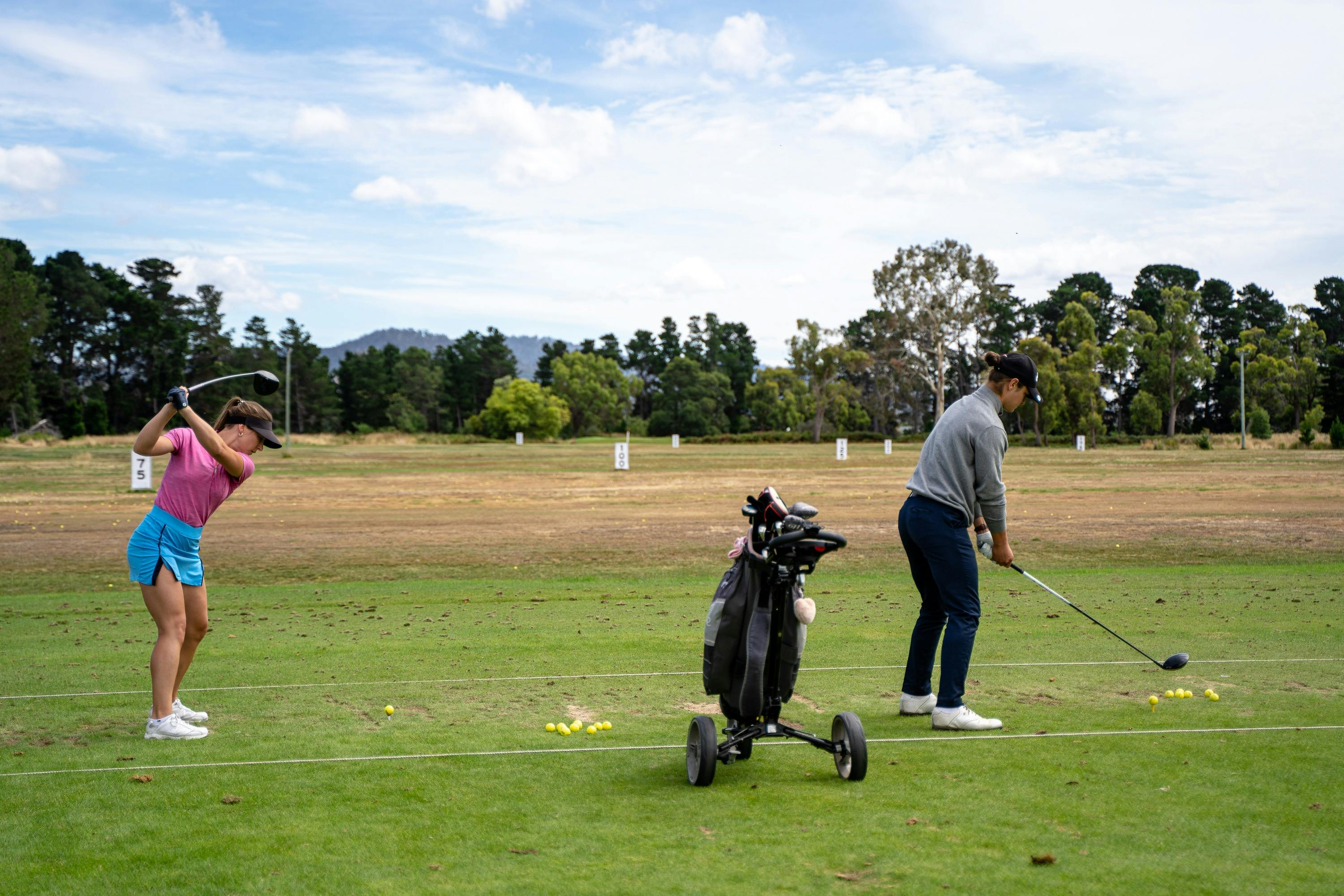 Female and male golfer practicing golf swing on driving range
