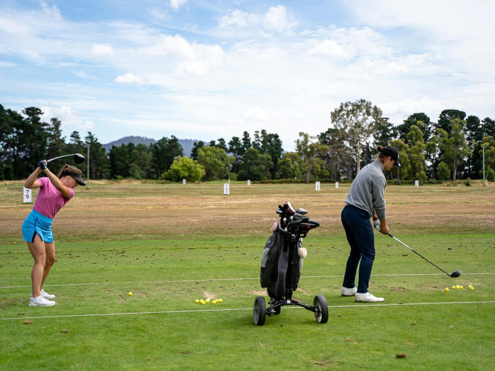 Female and male golfer practicing golf swing on driving range
