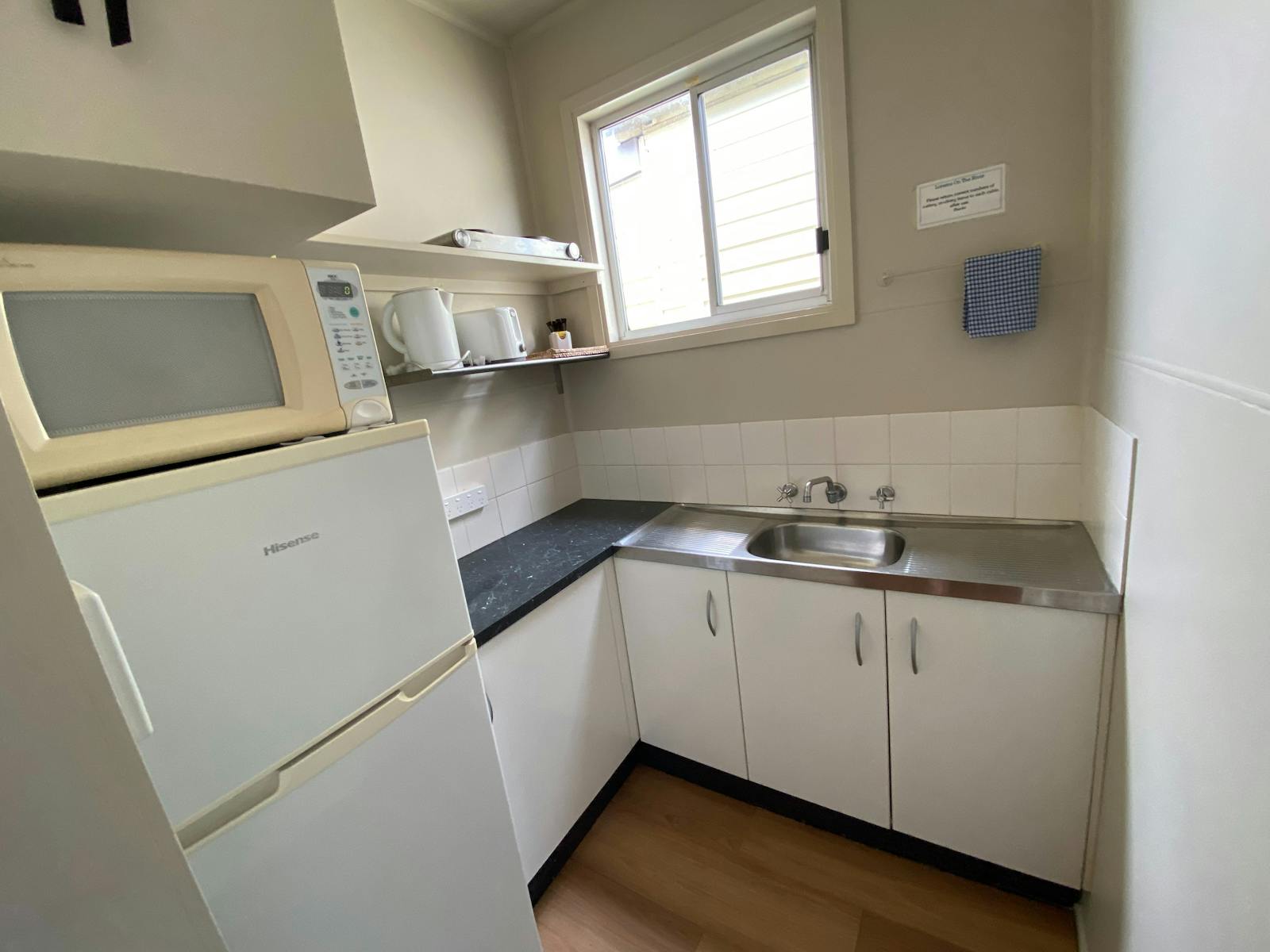 Small compact kitchen includes fridge, microwave, cooktop, crockery & cutlery