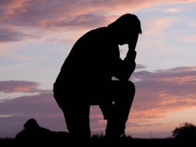 Silhoutte of a man kneeling down on one knee with his head in his hand as a symbol of  remembrance