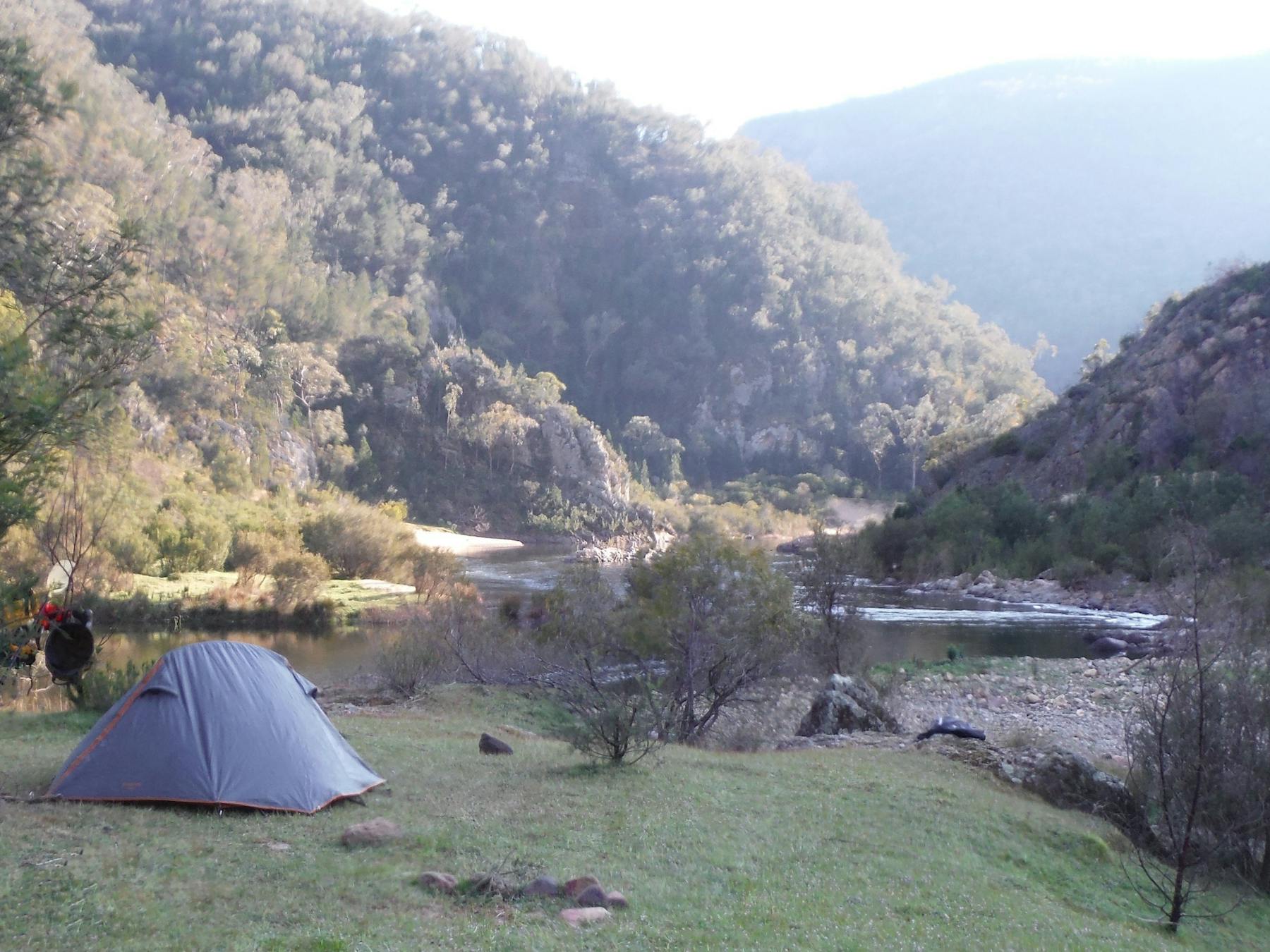 A tent is in the foreground on the edge of the Snowy River, beautiful mountains in the background