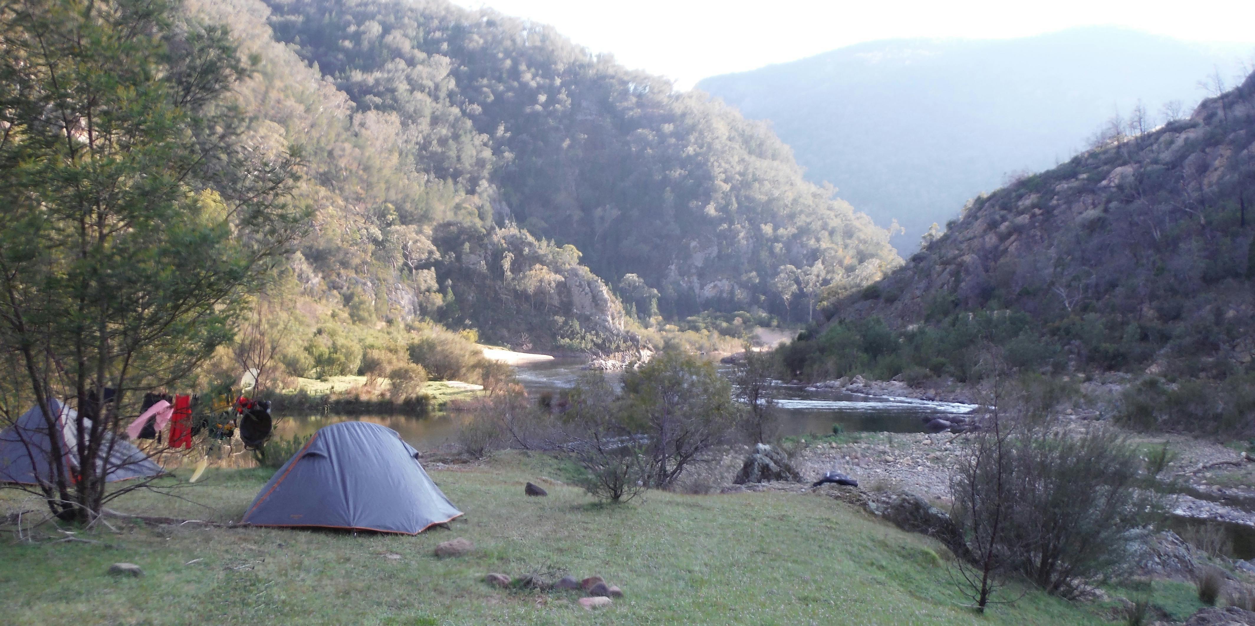A tent is in the foreground on the edge of the Snowy River, beautiful  mountains in the background