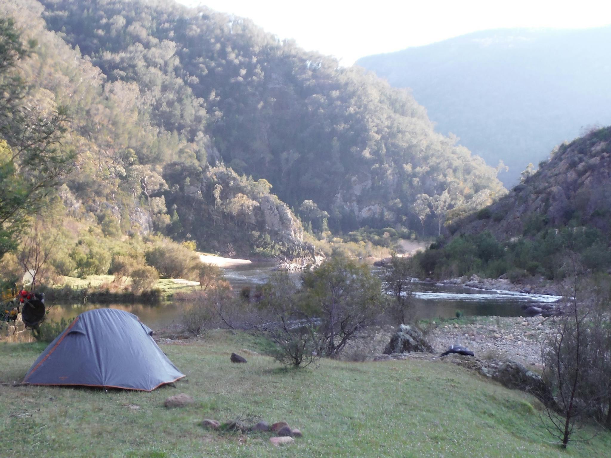 A tent is in the foreground on the edge of the Snowy River, beautiful  mountains in the background