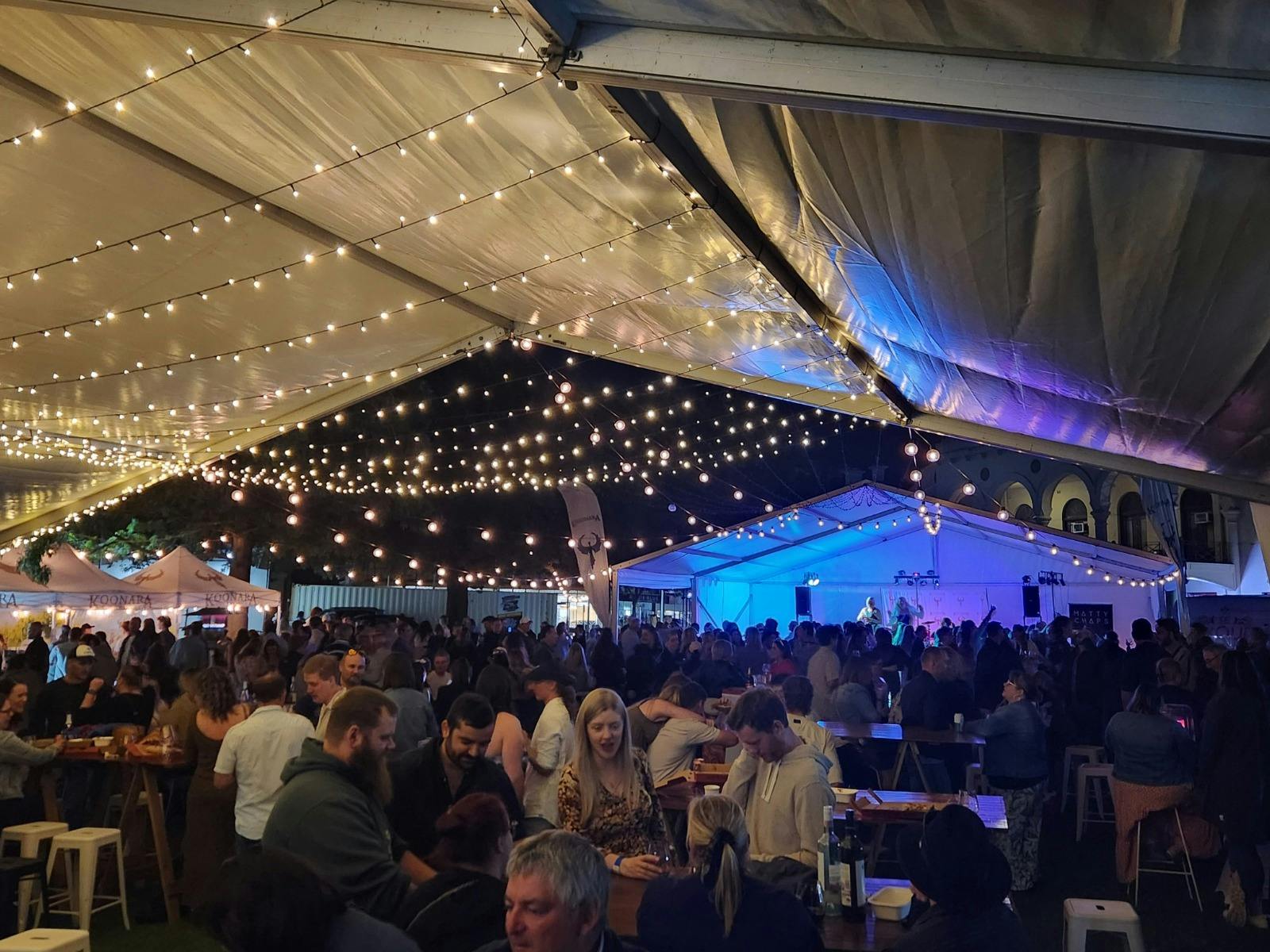 marquee at summer fiesta with crowd underneath, lit up by fairy lights and stage lighting