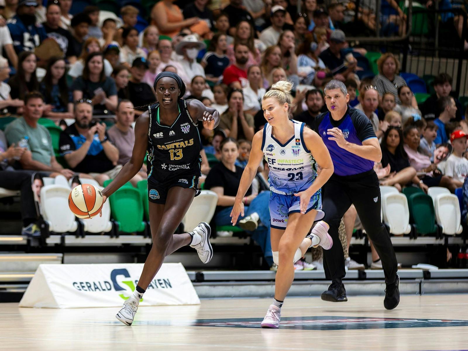 Basketball player runs down the court with defender in tow.
