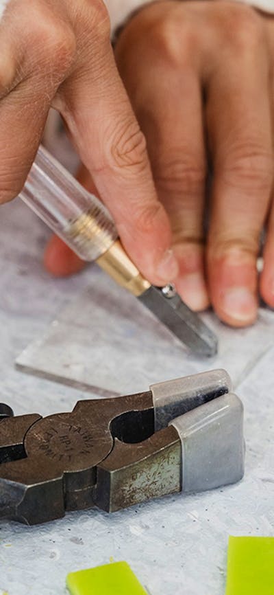 Childs hand cutting a piece of glass with special tools and matt