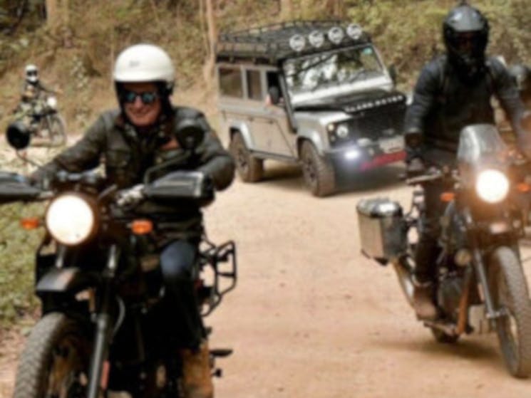 Landrovers and motorcycles driving down a dirt road