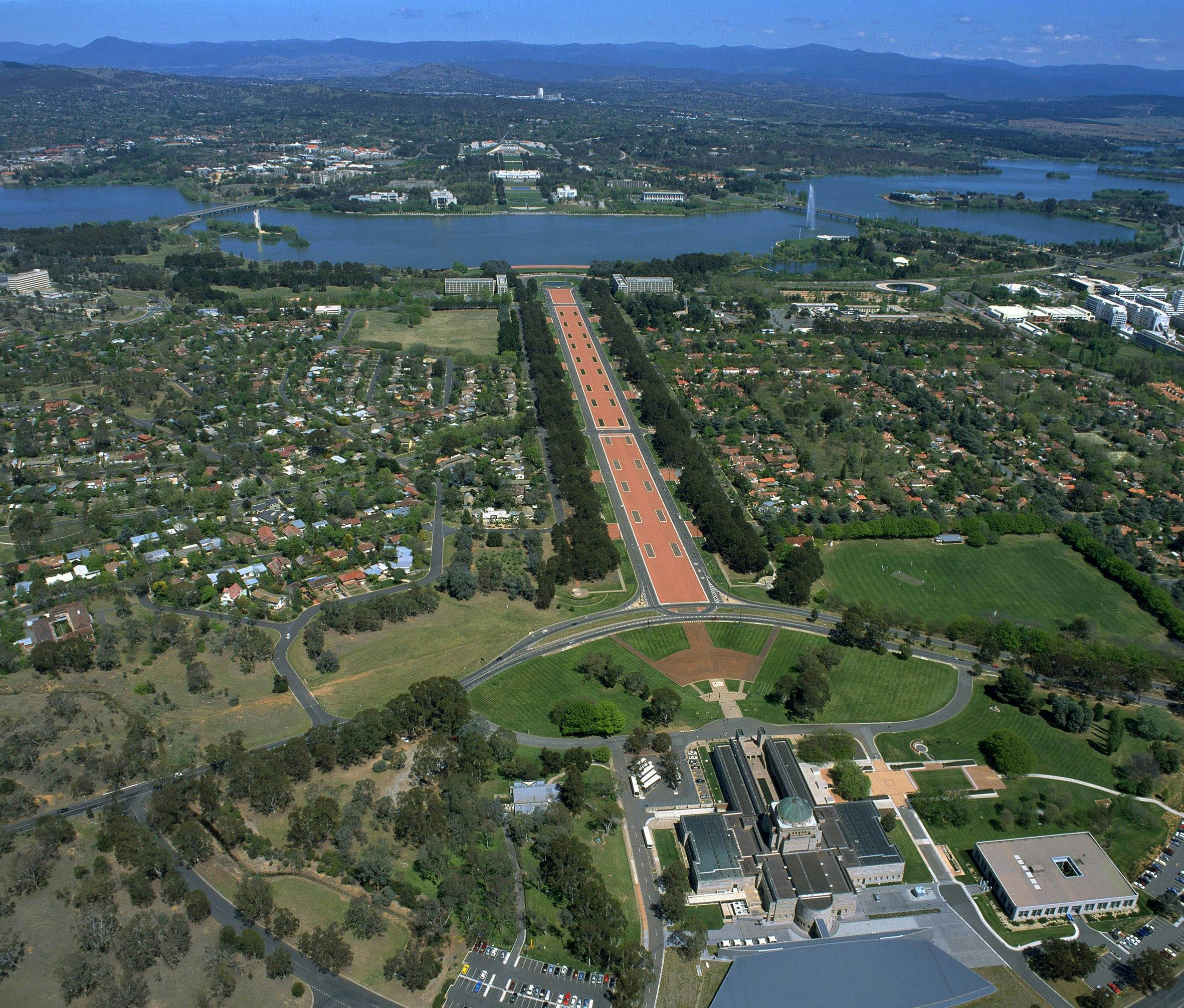 Aerial view of buildings, grassed areas, long promenade and lake.