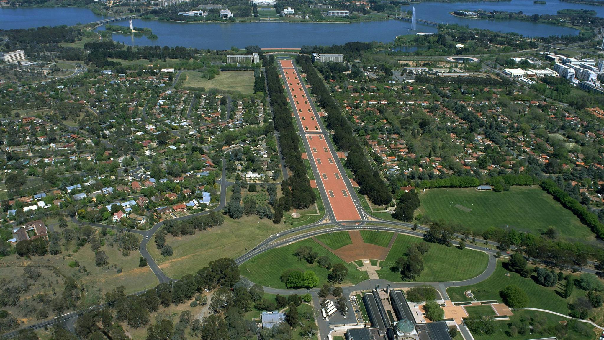 Aerial view of buildings, grassed areas, long promenade and lake.