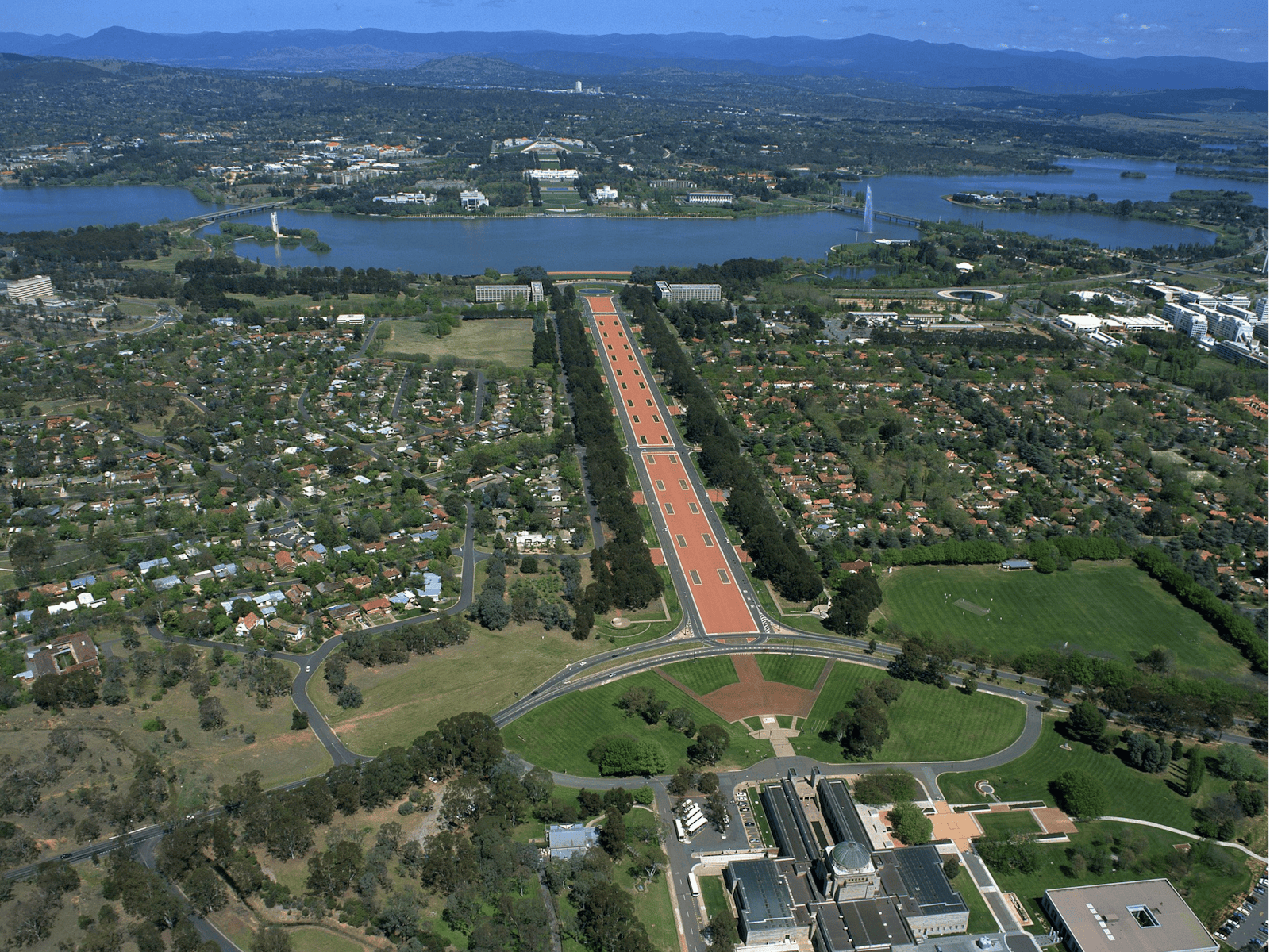 Aerial view of buildings, grassed areas, long promenade and lake.