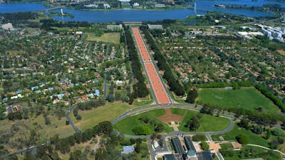 Aerial view of buildings, grassed areas, long promenade and lake.