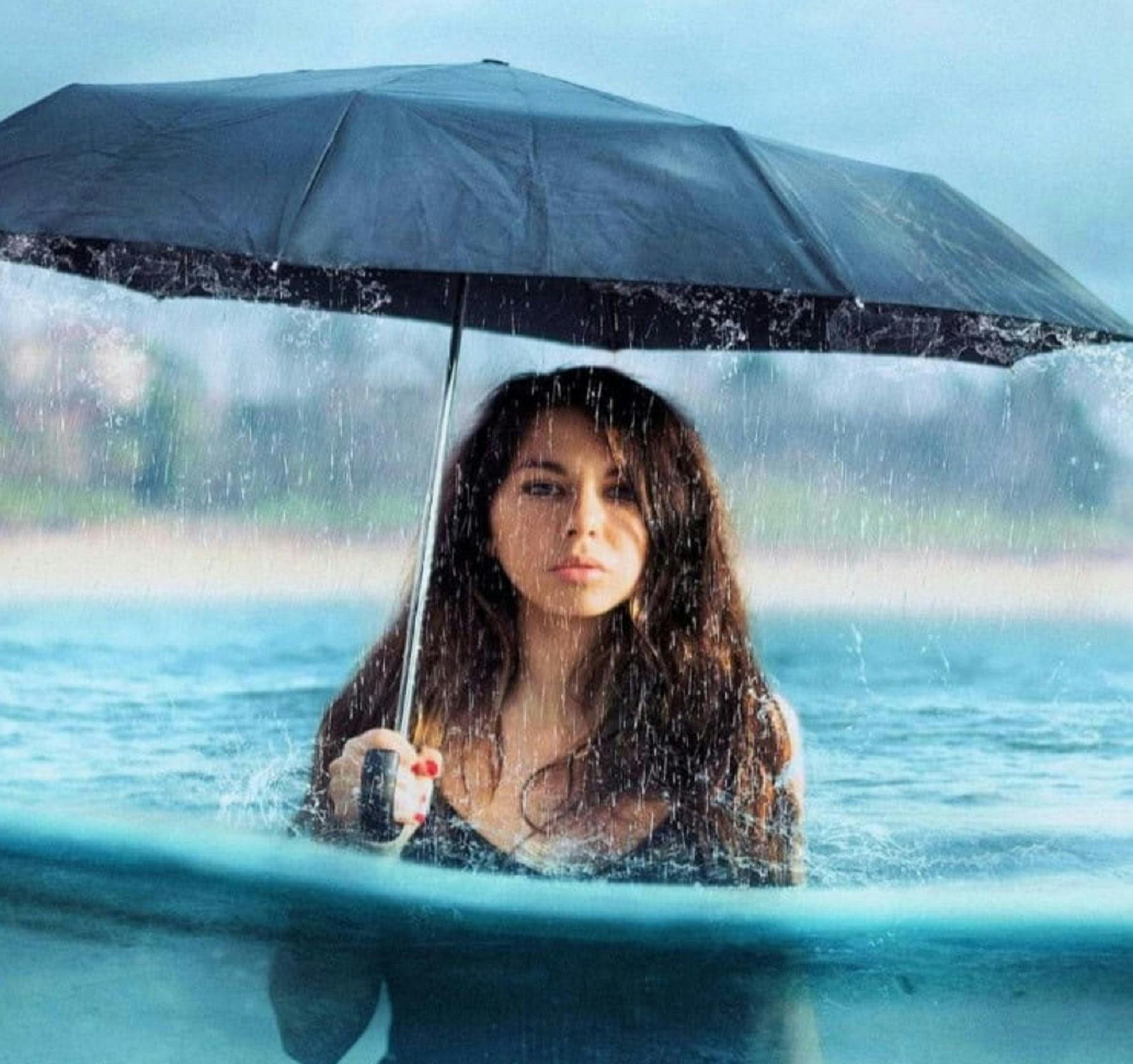 Woman standing in the sea with an umbrella (in the rain)