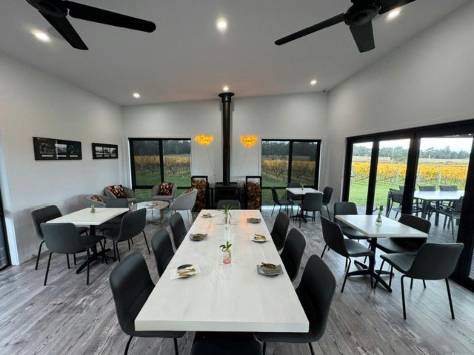Tables and chairs set up in front of a fireplace inside a cellar door overlooking grape vines
