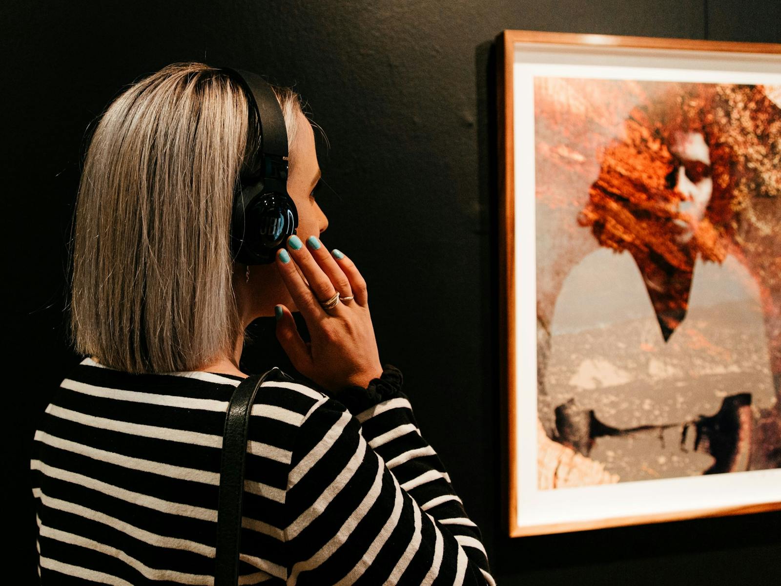A woman viewing a photographic work by Jahkarli Romanis, while listening to audio through headphones