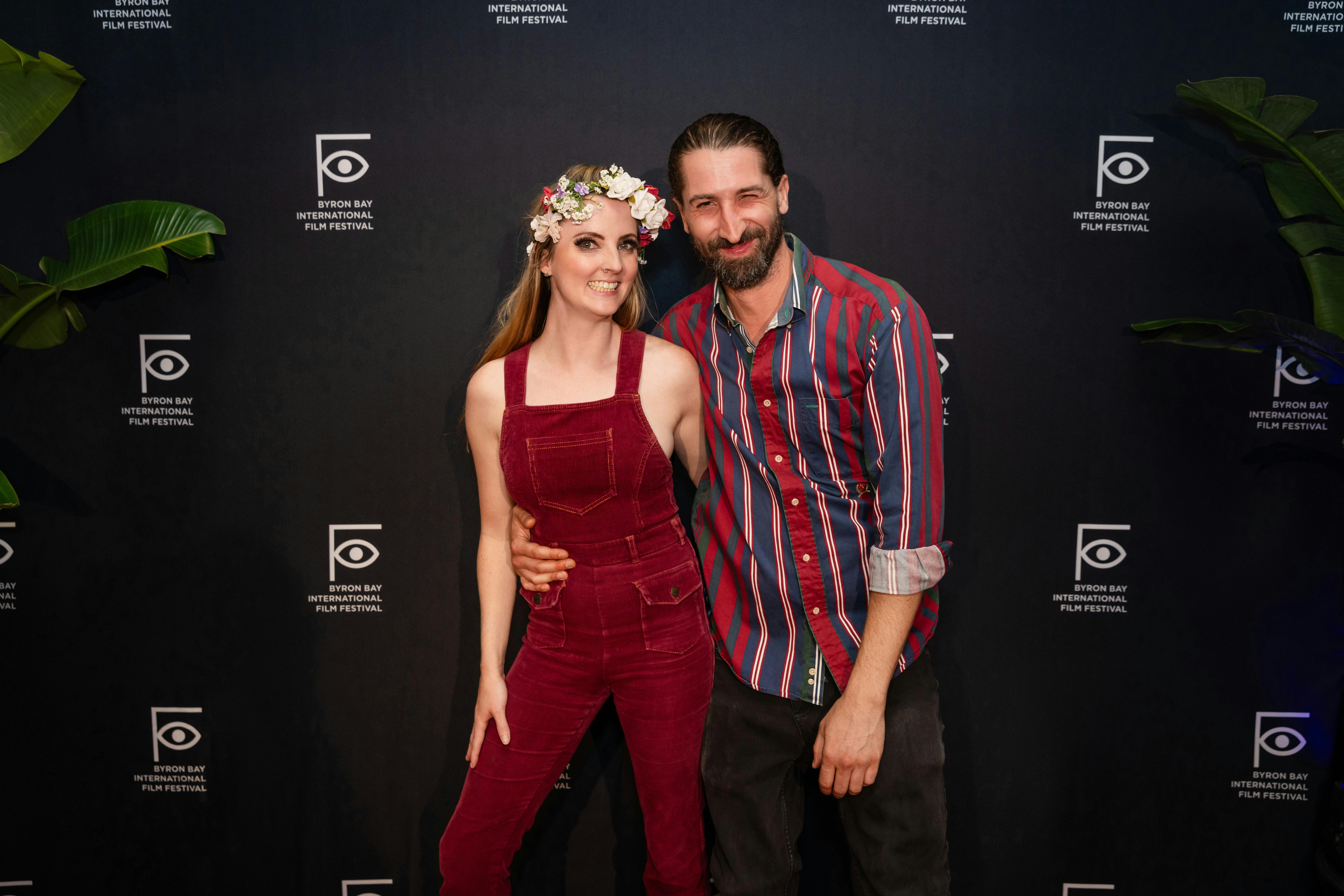 A woman and a man dressed in Aquarius Festival theme are standing in front of the media wall