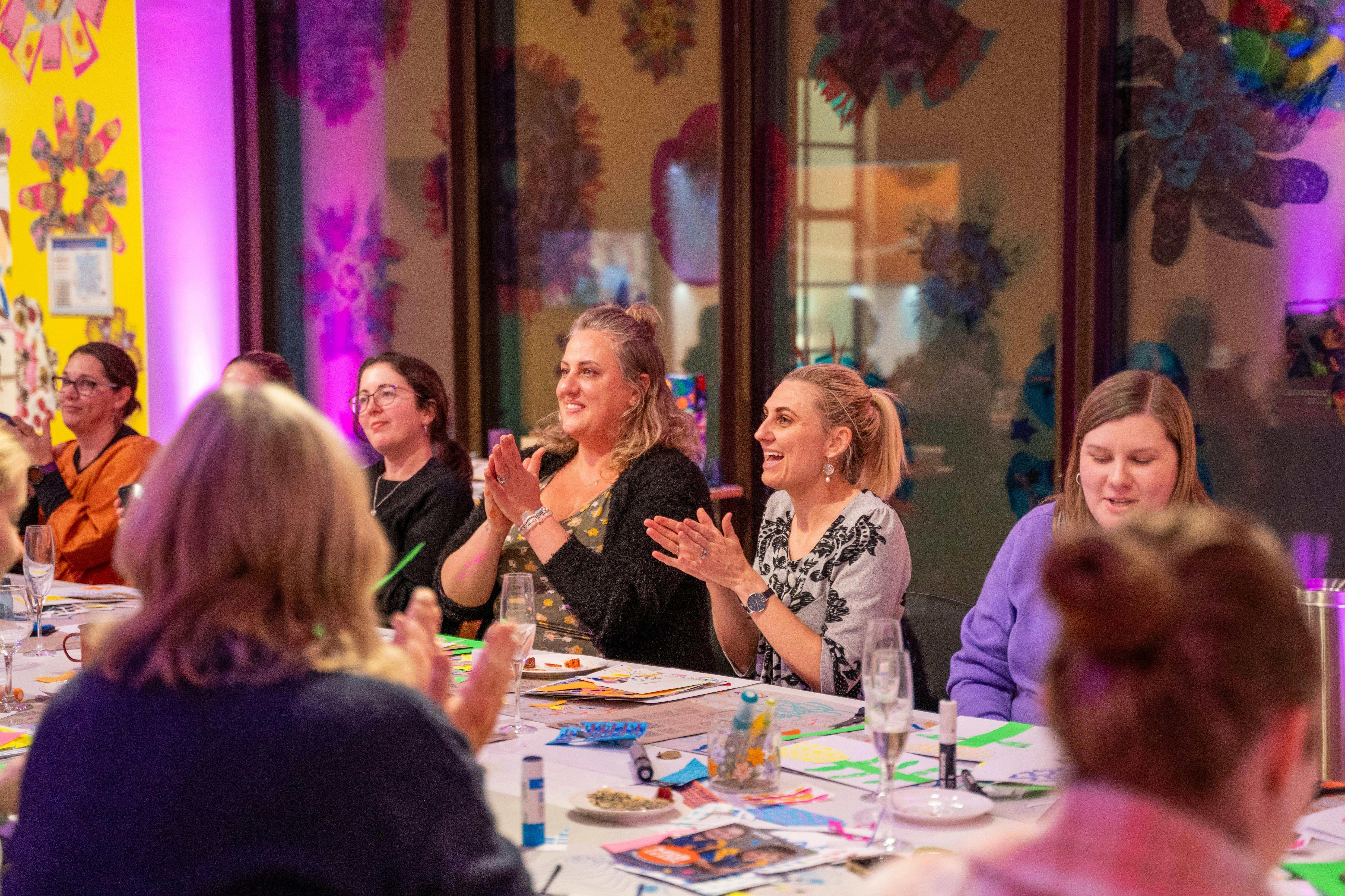 Crafty Party guests sitting at the workshop table, clapping, smiling and enjoying the event.