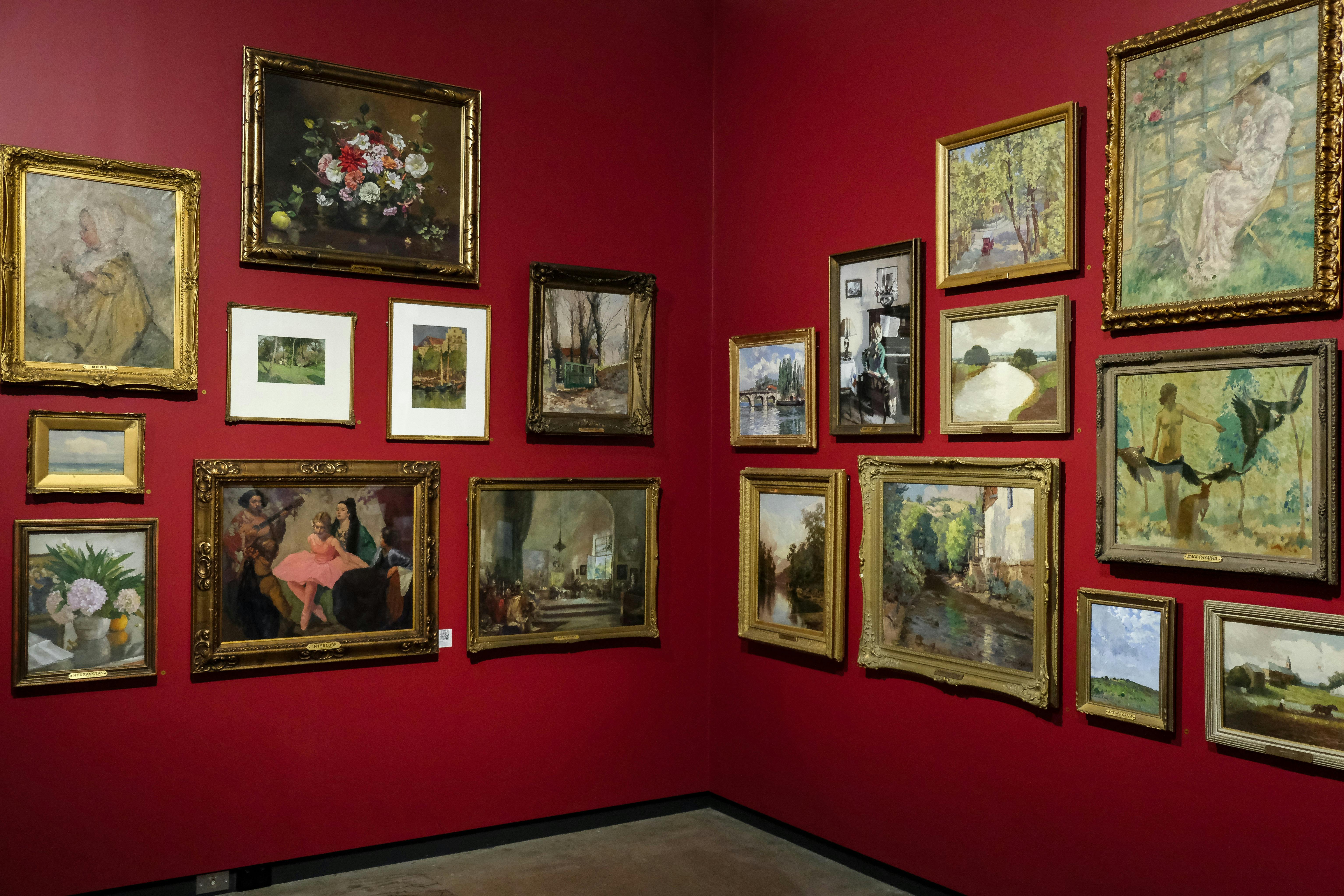 Kunstwerke in reich verzierten Rahmen hängen an einer roten Wand