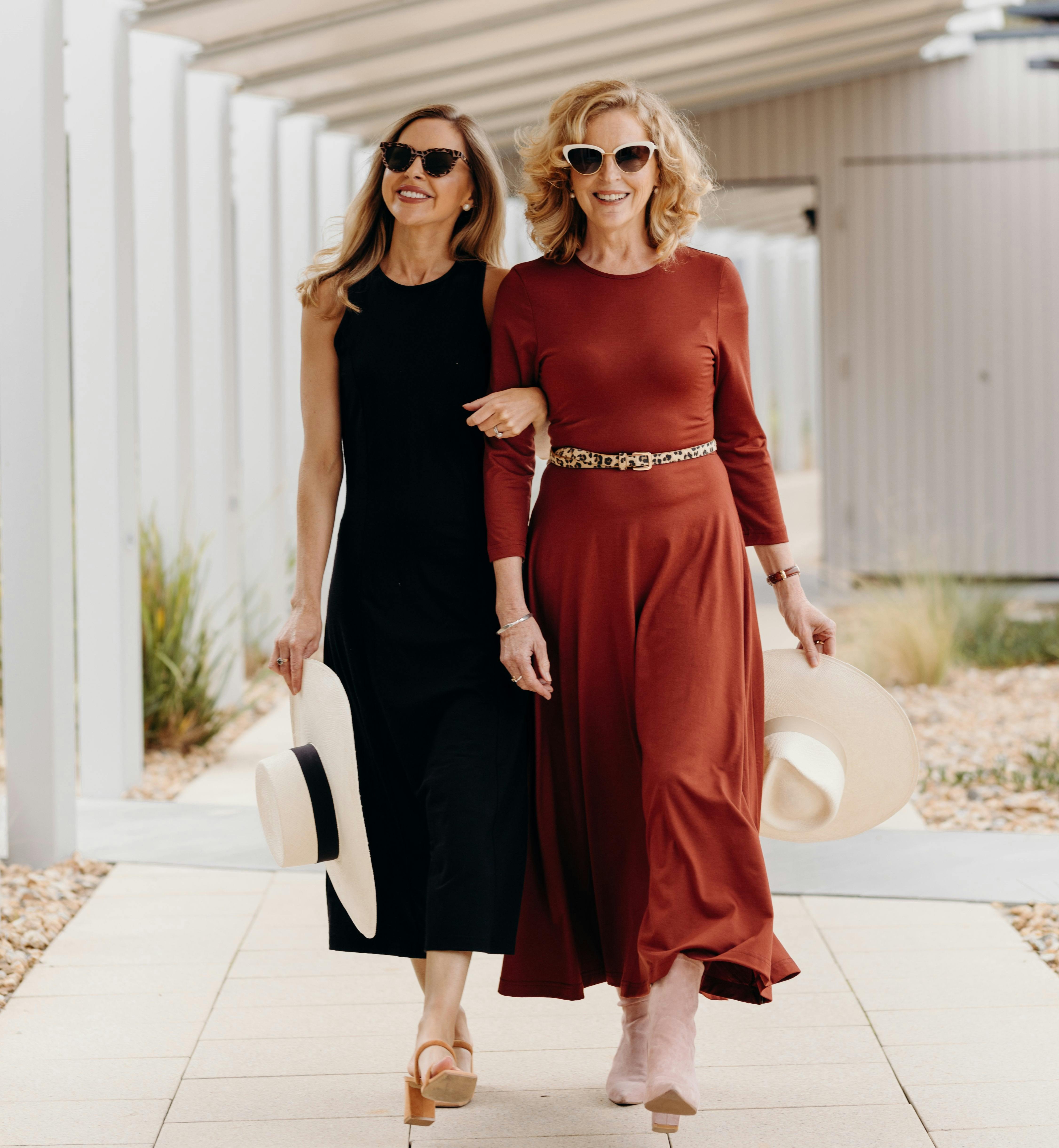 2 women walking wearing merino dresses, one in black, one in Shiraz red