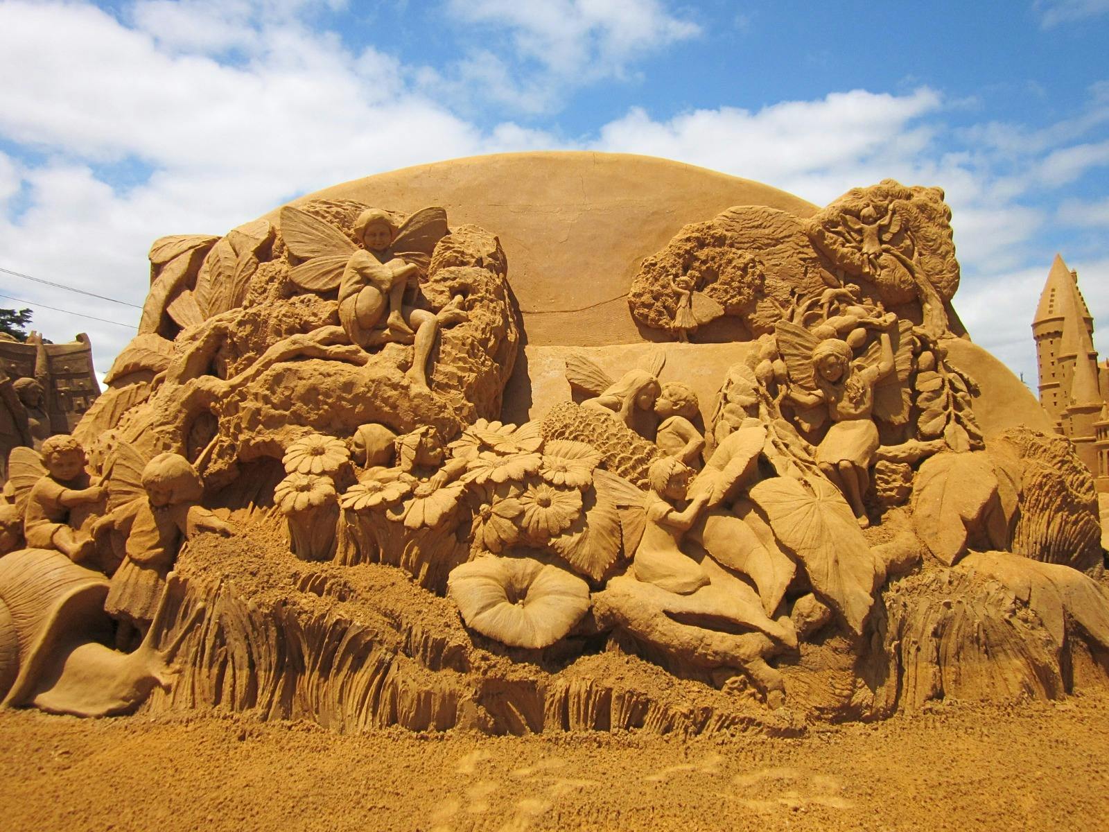 Intricate sand sculpture of fairies, flowers, and a castle tower.