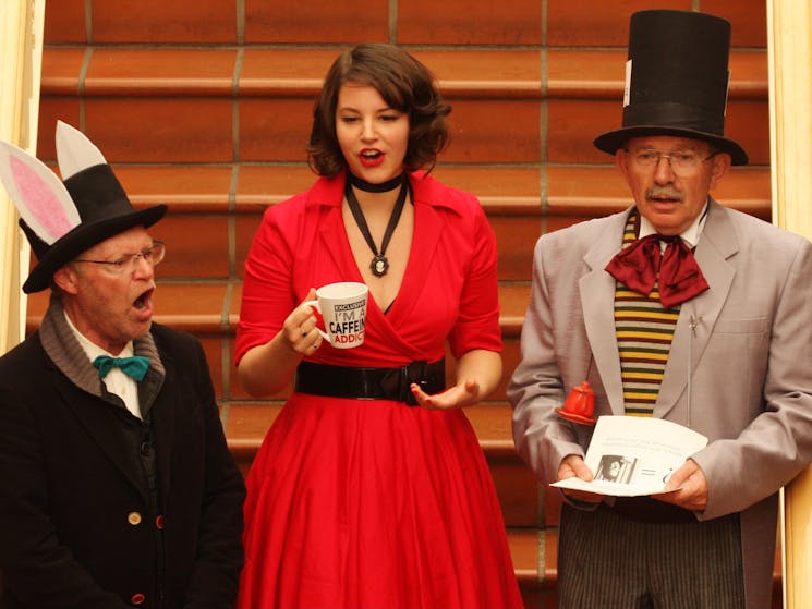 Three singers dressed as characters from Alice in Wonderland on flight of stairs.