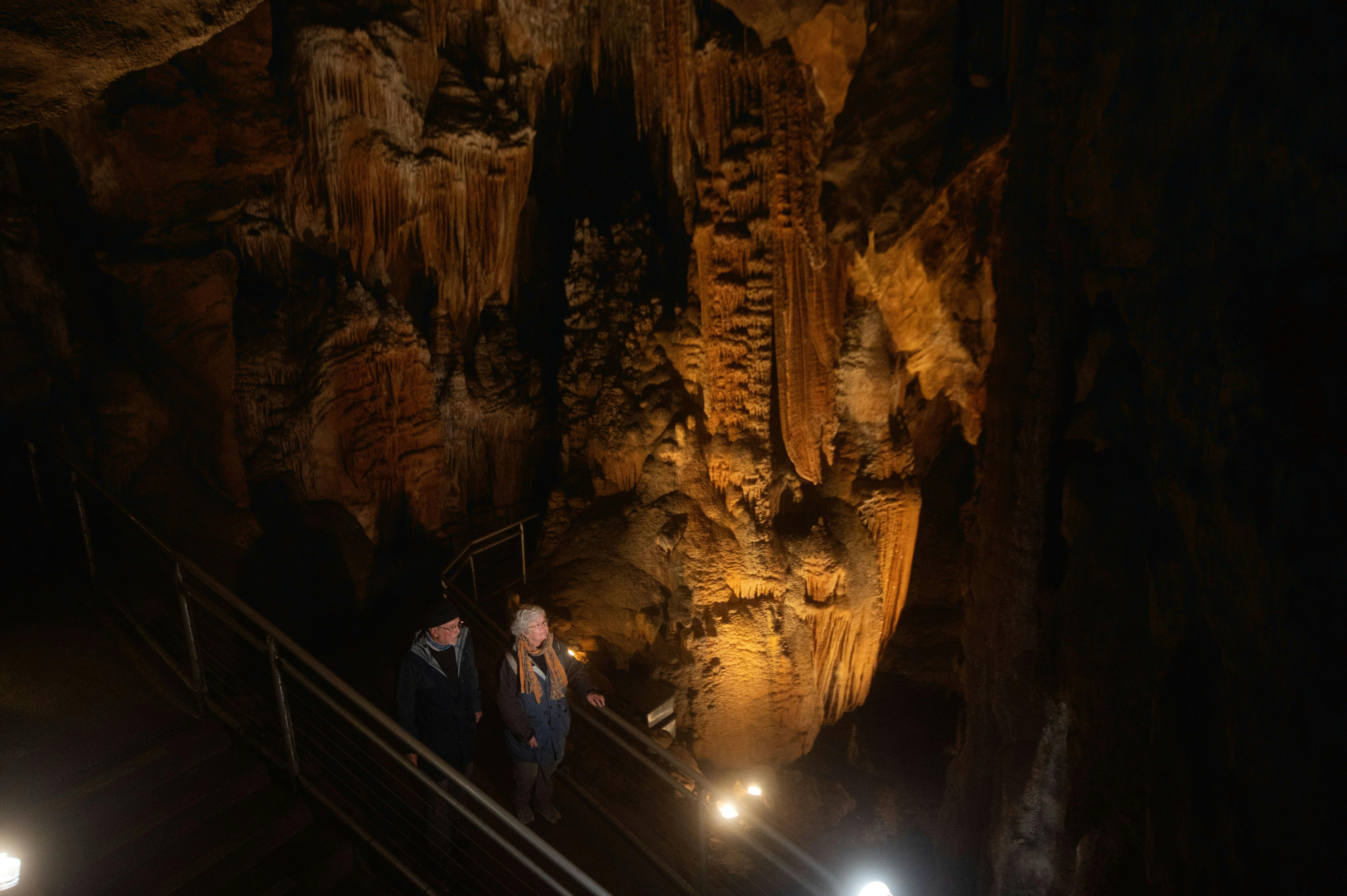 two people stnding behind a railing overlooking a vast cave interior and cave formations